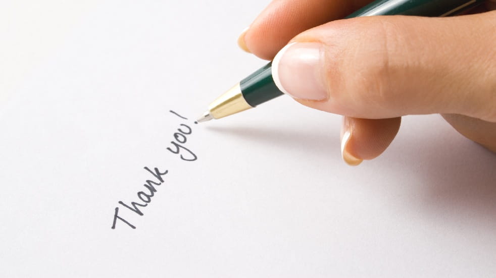 person writing thank you on piece of paper